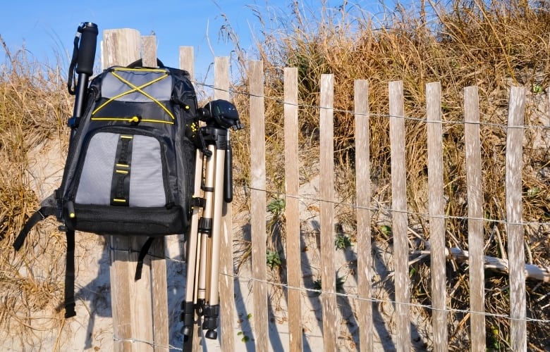 A camera bag with a tripod hangs from a wood fence