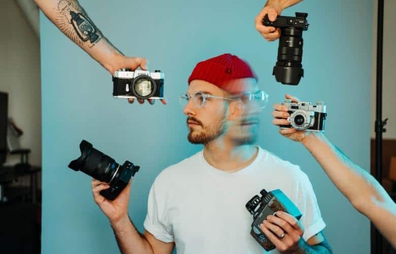 A photographer is surrounded by cameras and is trying to decide which one to use