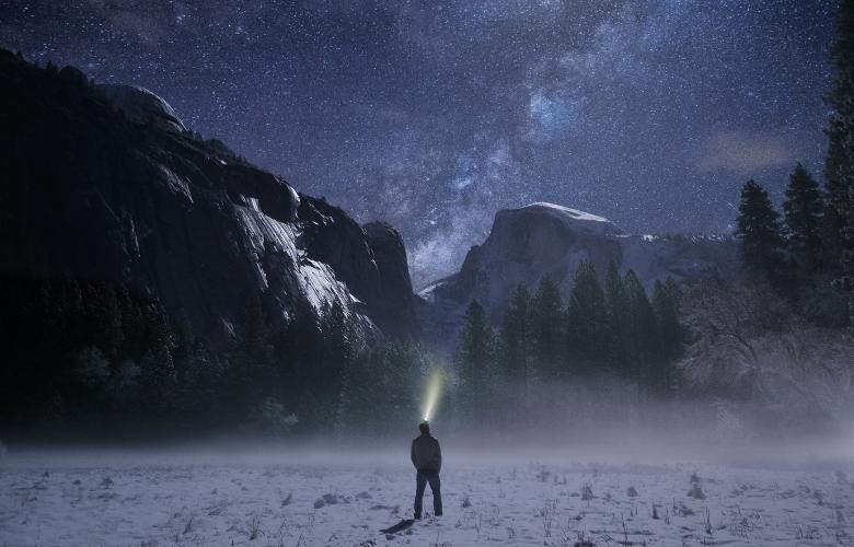 A man stands in a field, gazing up at the star-studded night sky.