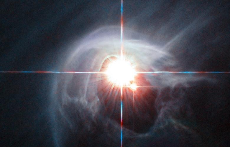 In this image taken by the NASAESA Hubble Space Telescope, two stars shine through the center of a ring of cascading dust.