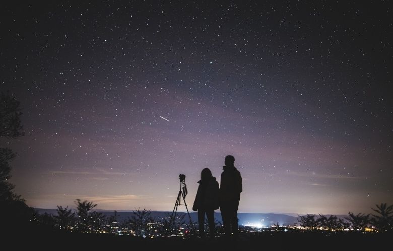 A couple looks up at a shooting star in the dark night sky.